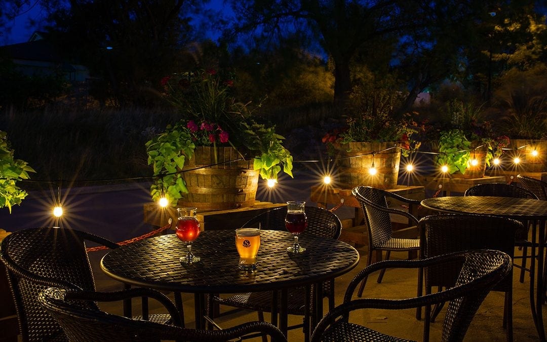 Picture at night of outside patio with beer on tables. Satire Brewing Company